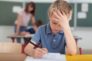 young boy frustrated while doing work in his classroom